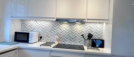 A modern kitchen with white cabinetry, a microwave, a toaster, and a sink.