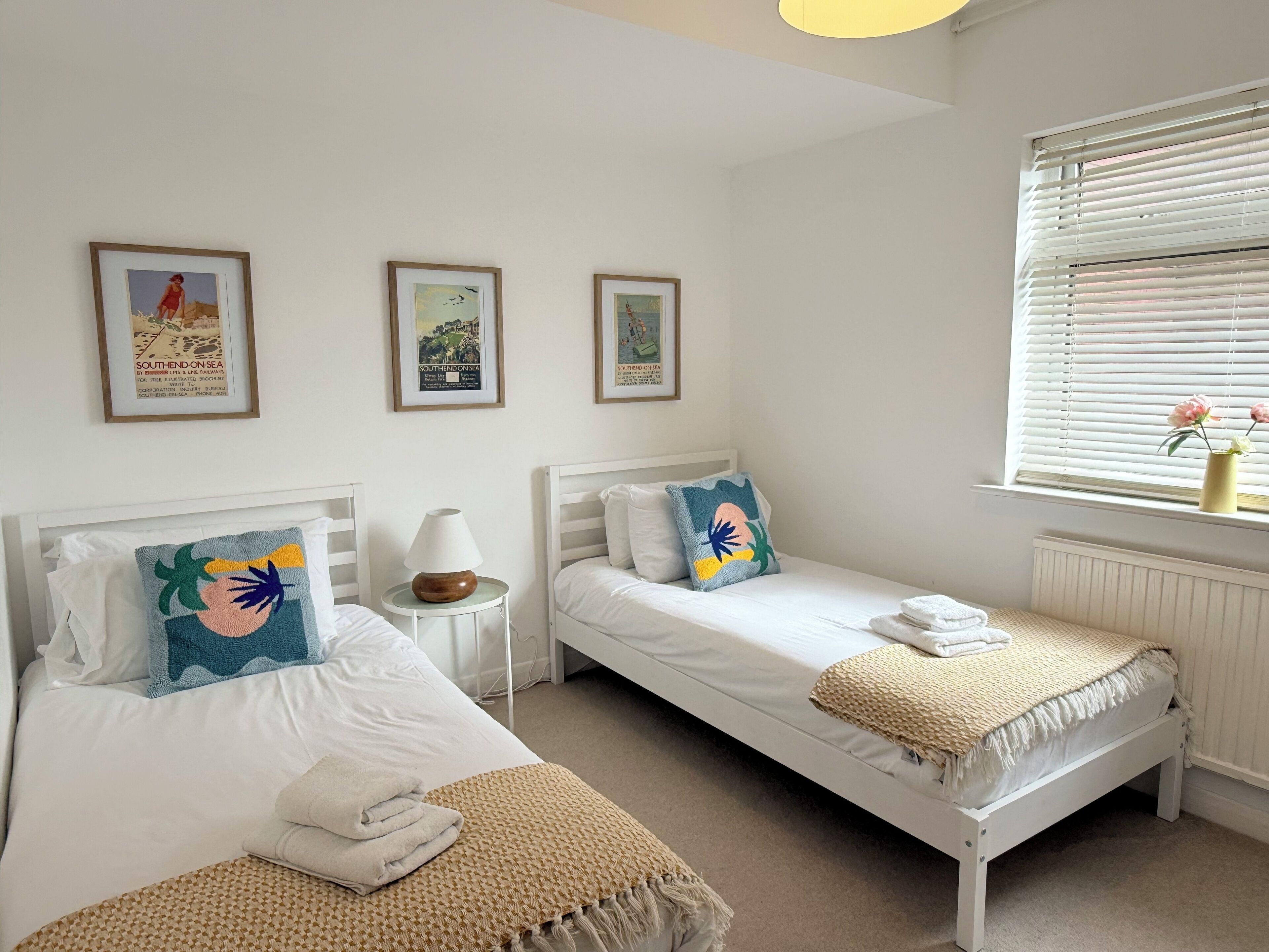 Een hotelkamer met twee enkele bedden, een klein nachtkastje met een lamp en een raam met jaloezieën.