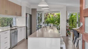 A modern kitchen with a central island, stainless steel appliances, and a view of greenery outside. - Sunshine on Saltwater (Kingscliff)