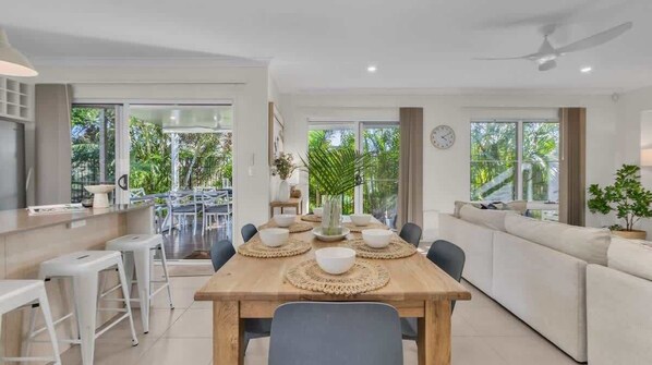 A modern kitchen with a dining area, large windows, and a view of greenery.