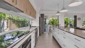 A modern kitchen with a central island, stainless steel appliances, and a view of the outdoor garden. - Sunshine on Saltwater (Kingscliff)