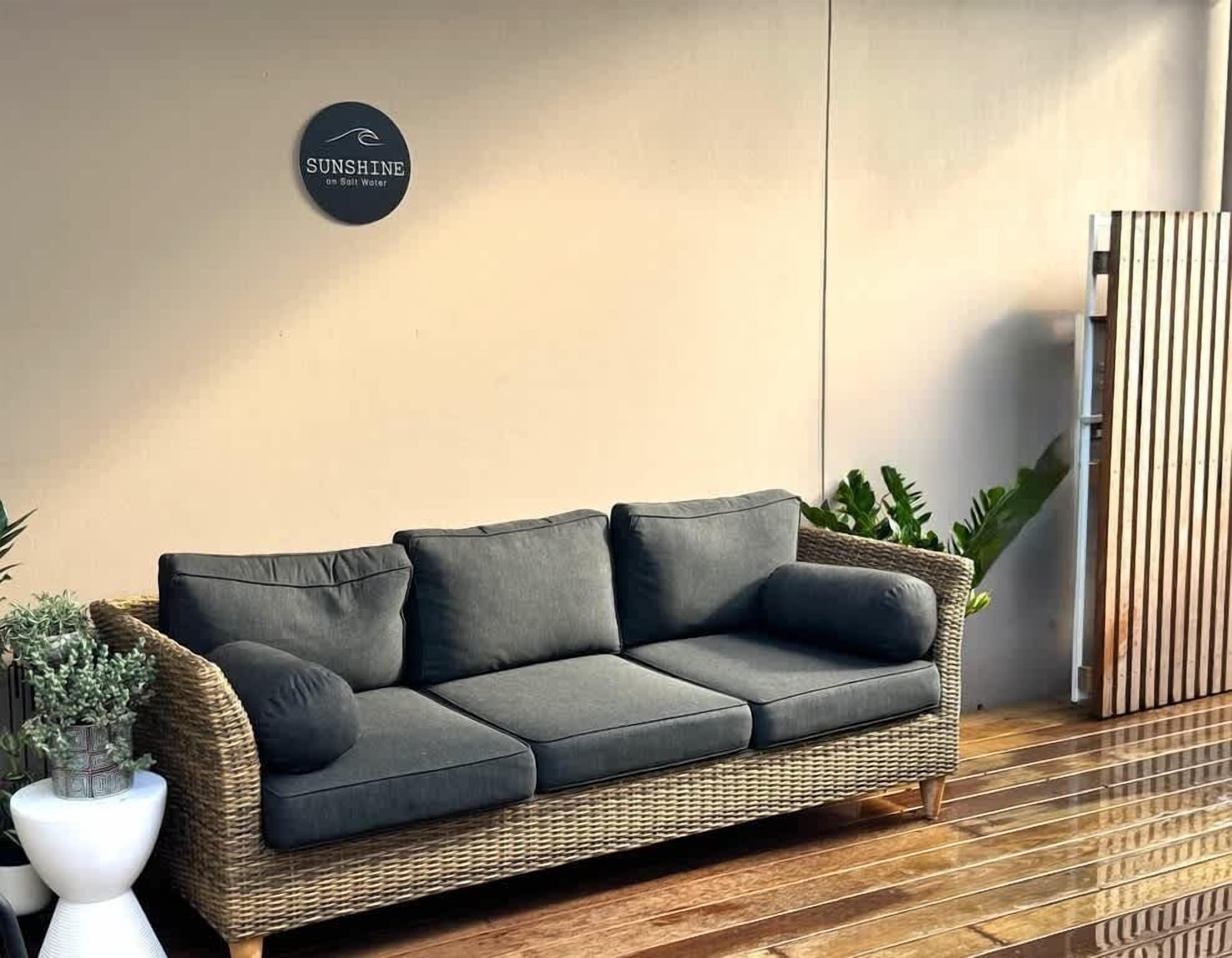 Ein Korbsessel mit Kissen, eine Topfpflanze und ein an der Wand befestigtes Schild.