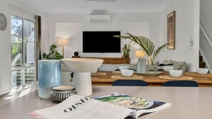 A modern living room with a dining area, a flat-screen TV mounted on the wall, and a magazine on the table. - Sunshine on Saltwater (Kingscliff)
