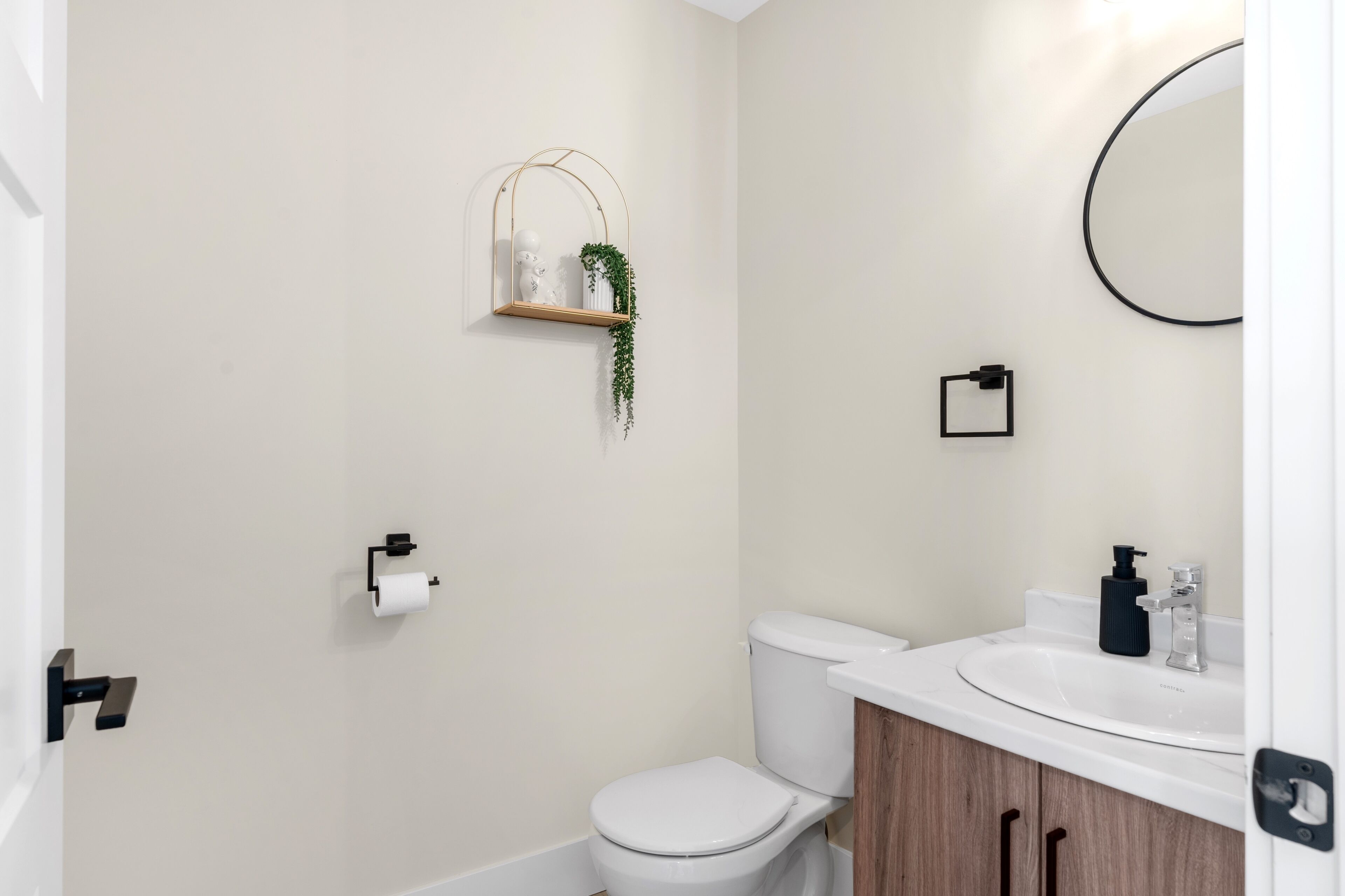 Ein Badezimmer mit Toilette, Waschbecken, Spiegel, Handtuchhalter und einem kleinen Regal mit einer Pflanze.
