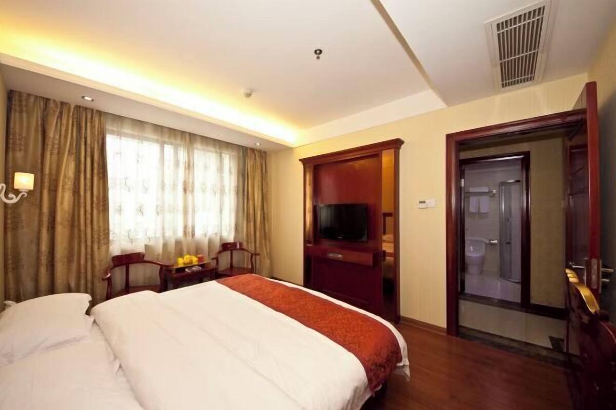A hotel room with a bed, a television, a desk, and a bathroom visible through an open door.