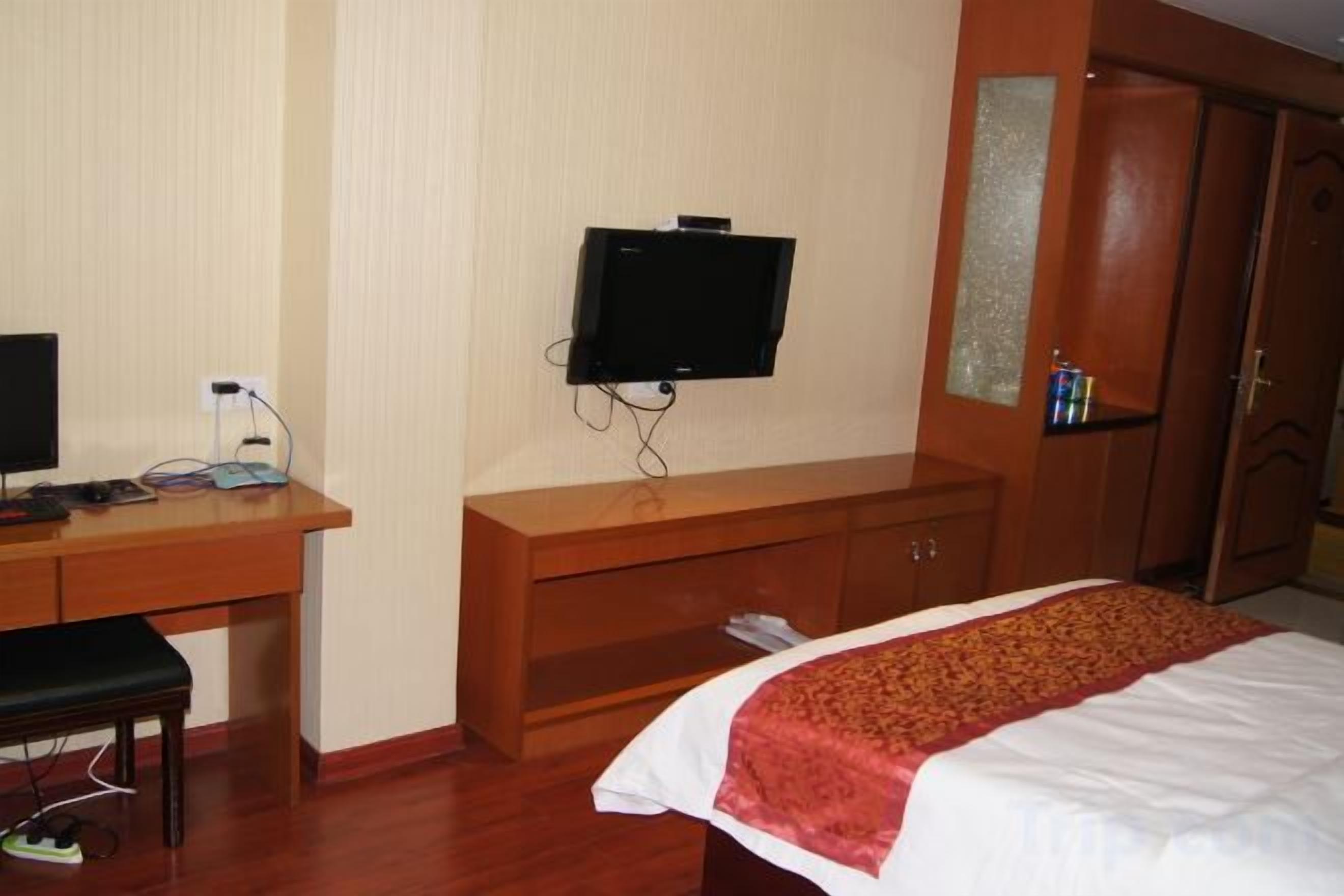 A hotel room with a bed, a desk with a computer, a television, and a wardrobe.
