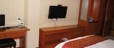 A hotel room with a bed, a desk with a computer, a television, and a wardrobe.