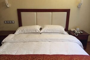 Quarto de hotel com uma cama grande, cabeceira de madeira, mesa de cabeceira com telefone e tomada na parede.