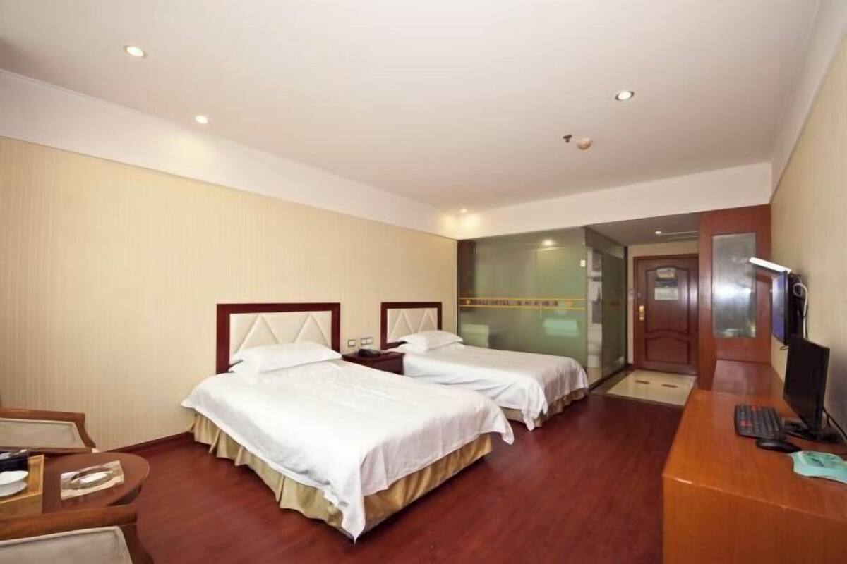 A hotel room with two beds, a desk with a computer, and a door leading to a hallway.
