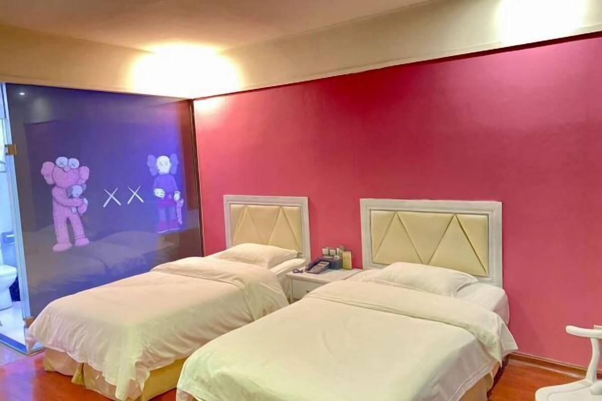A room with two beds, a red wall, and a large window.