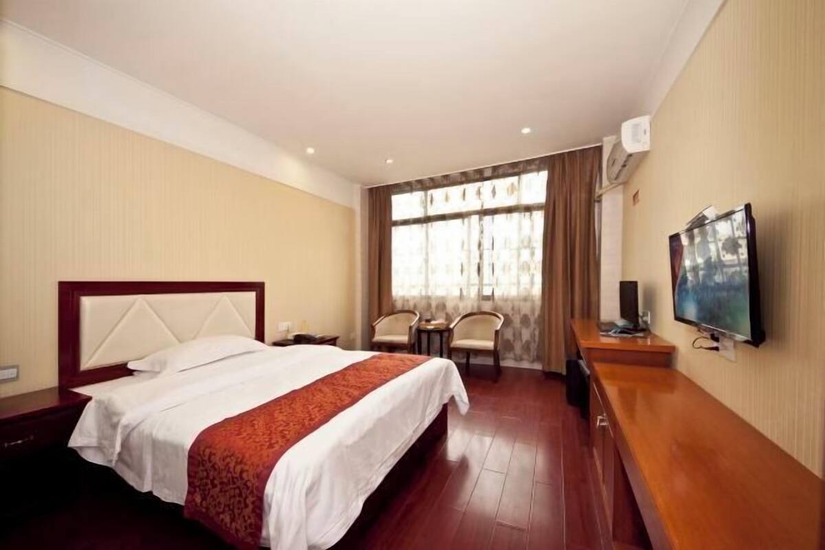 A hotel room with a bed, a TV, a desk, and a window with curtains.