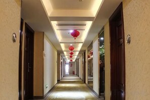 A hotel hallway with doors on both sides, red lanterns hanging from the ceiling, and a light-colored floor. - New Fali Hotel (Lianjiang)