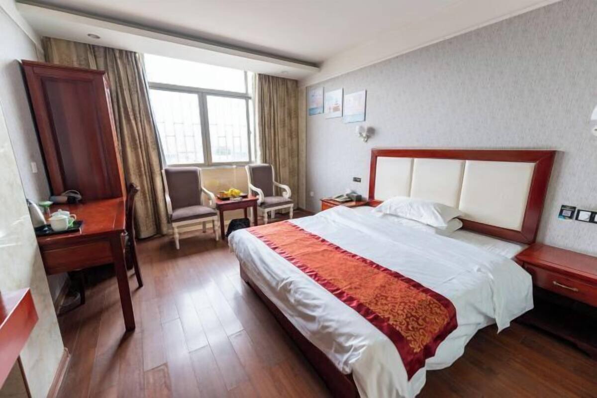 A hotel room with a large bed, a desk, a chair, a small table, and a window with curtains.
