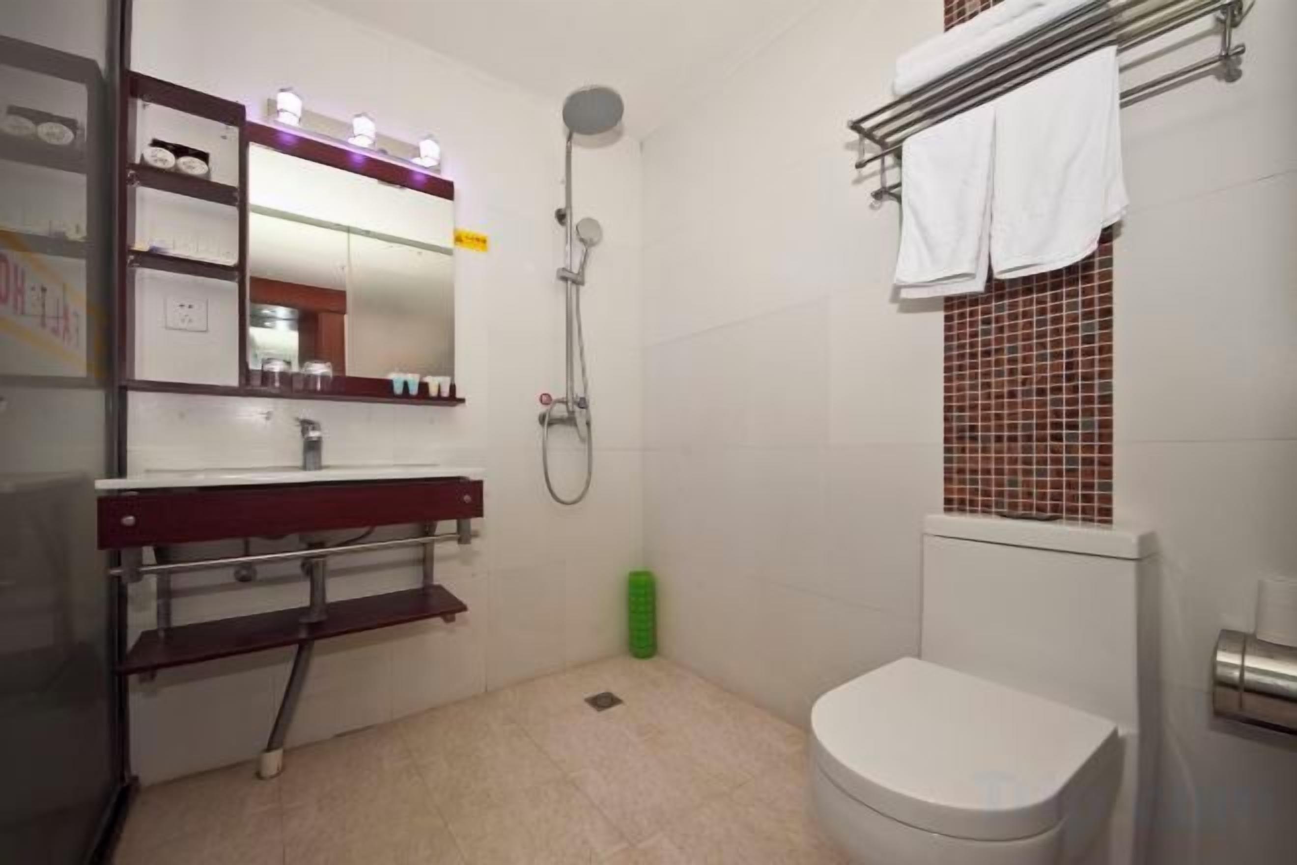 Egy fürdőszoba, amelyben WC, mosdókagyló, tükör, zuhanyzó és törölközőtartó található.