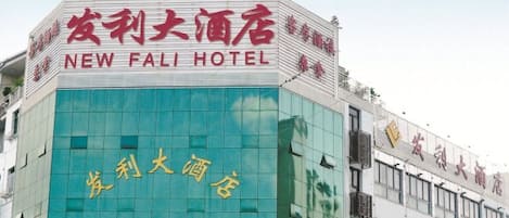 Un edificio de hotel con un letrero llamativo que dice 'NEW FALI HOTEL' en inglés y otra escritura.
