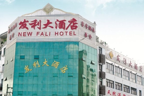 Un edificio de hotel con un letrero llamativo que dice 'NEW FALI HOTEL' en inglés y otra escritura.