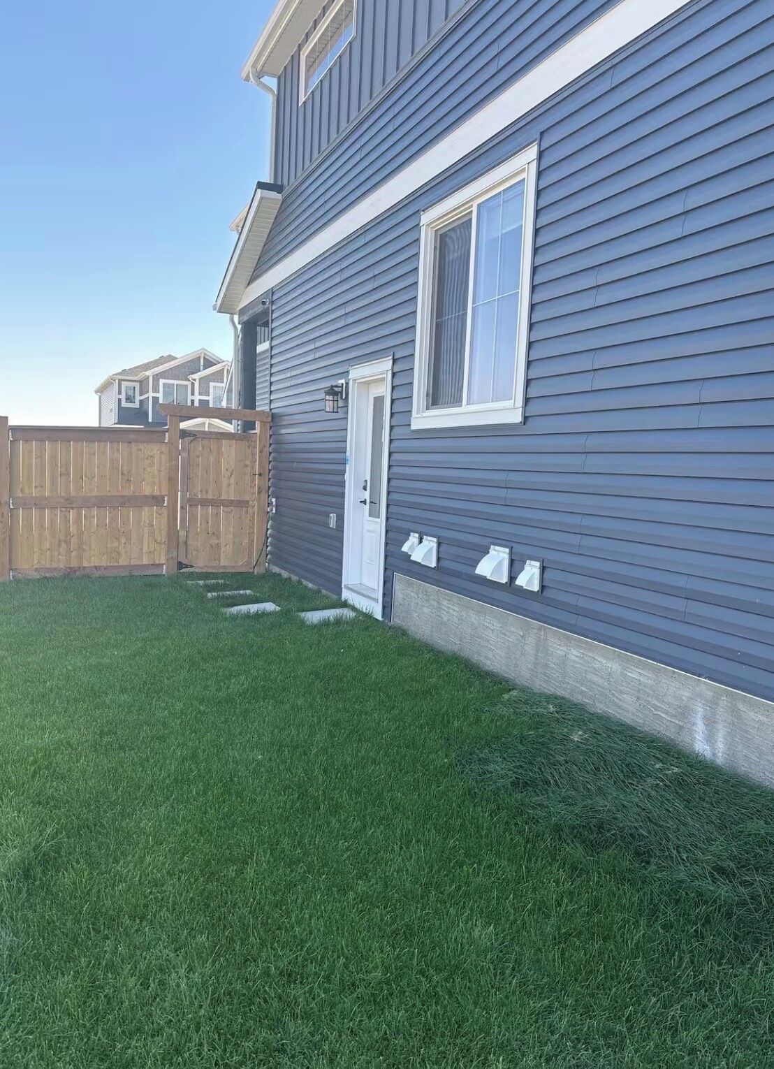 Una casa residencial con un césped bien cuidado, una cerca de madera y una puerta blanca.
