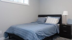 Ein Schlafzimmer mit Bett, Nachttisch, Lampe und Fenster.