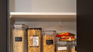 Ein Lagerbereich mit beschrifteten Behältern, die verschiedene Lebensmittel enthalten, darunter Haferflocken, Cornflakes und eine Müslimischung.