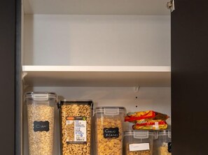 Storage area with labeled containers for OAT, CLIP, and CORN FLAKES, plus cereal bars.