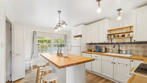 Une cuisine moderne avec des meubles blancs, un îlot central en bois et des tabourets de bar.