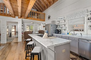 A spacious kitchen with a marble island, wooden ceiling beams, and a view to the outdoors. - kingisher river cabin (Murphy)