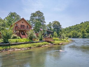 A lodge with a deck overlooking a river, surrounded by lush greenery. - kingisher river cabin (Murphy)