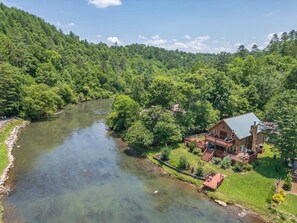 A lodge by a river with a deck and outdoor seating. - kingisher river cabin (Murphy)