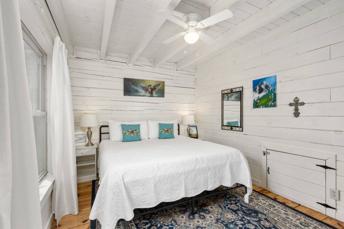 A bedroom with a bed, a ceiling fan, a window with curtains, and a patterned rug.