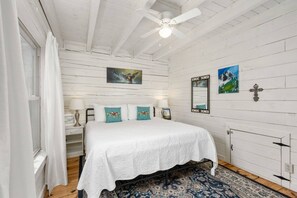A bedroom with a bed, a ceiling fan, a window with curtains, and a patterned rug. - kingisher river cabin (Murphy)