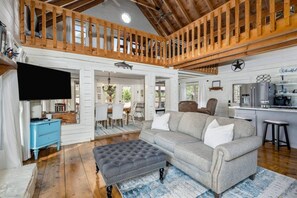 A spacious living area with a high ceiling, a grey sofa, a blue cabinet, and a kitchen area with a star logo. - kingisher river cabin (Murphy)