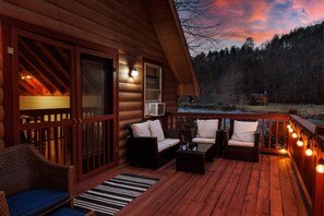A wooden deck with outdoor seating and a view of a forested area. - kingisher river cabin (Murphy)