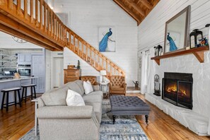 A spacious living room with a fireplace, a staircase, and a kitchen area. - kingisher river cabin (Murphy)