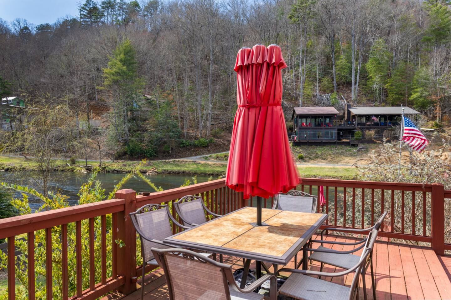 A deck with outdoor furniture, a red umbrella, and a view of a cabin and forest.