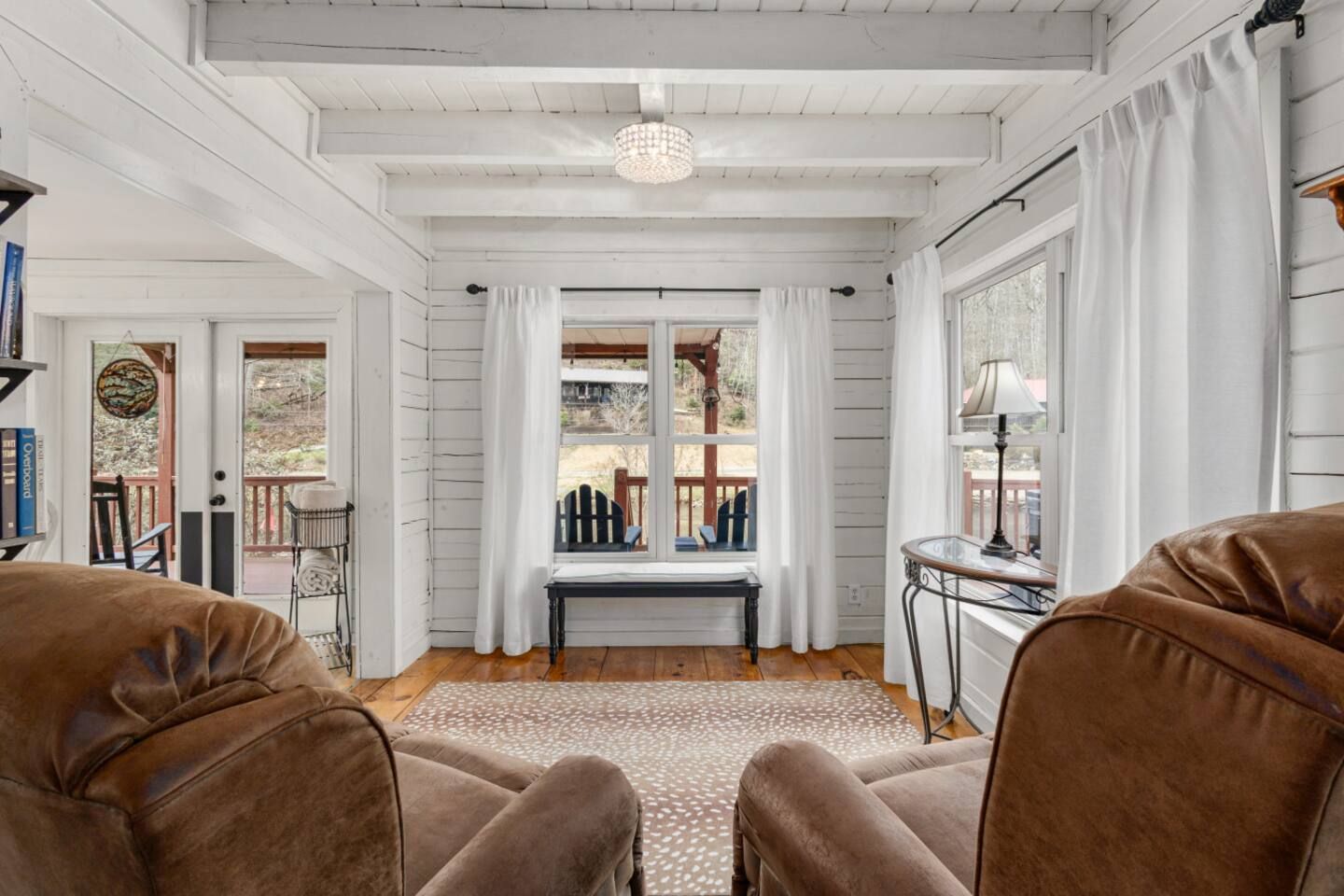 A room with a wooden ceiling, a bench, a table with a lamp, and two chairs.