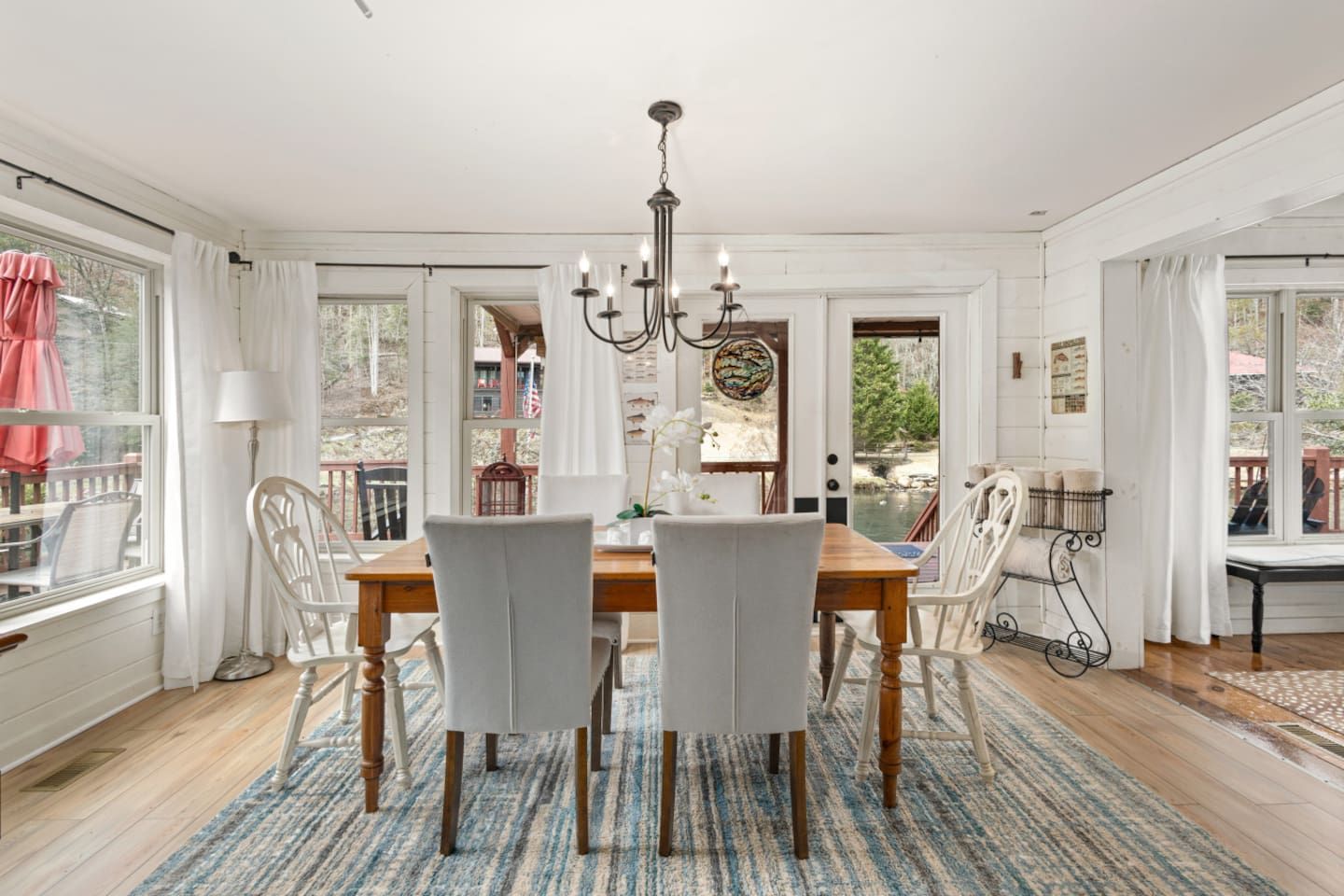 A dining room with a wooden table, white chairs, a chandelier, and a view through the glass door.