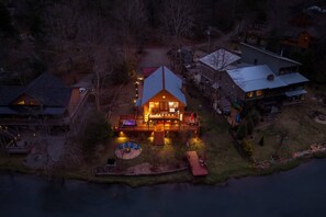 A large, multi-story house with a prominent front deck and a dock extending into a body of water. - kingisher river cabin (Murphy)