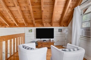 A cabin interior with a wooden ceiling, a flat-screen TV, white upholstered chairs, and a window with curtains. - kingisher river cabin (Murphy)