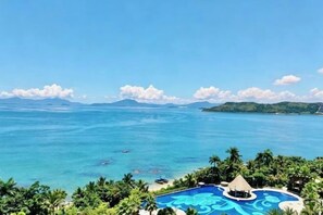 Un resort con piscina, exuberante vegetación tropical y vistas al océano.