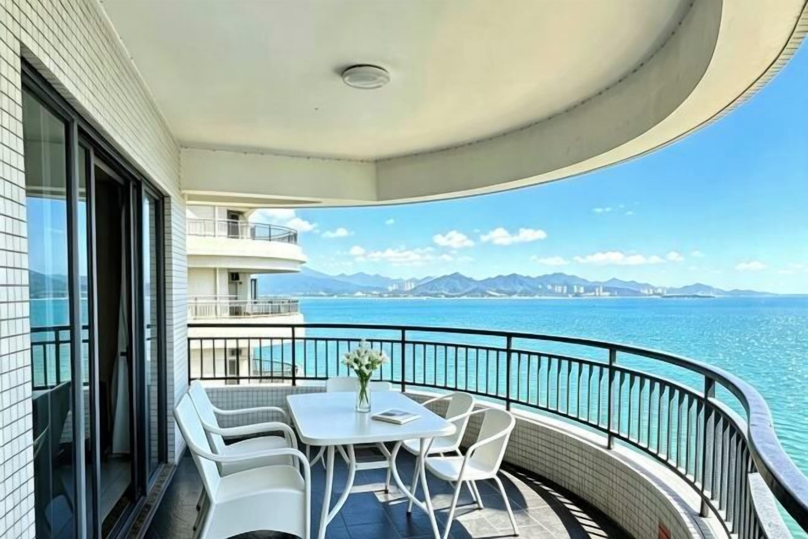 A balcony with a table and chairs, overlooking a body of water and distant mountains.