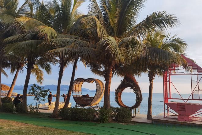 A beach area with palm trees, a heart-shaped sculpture, and a red structure.