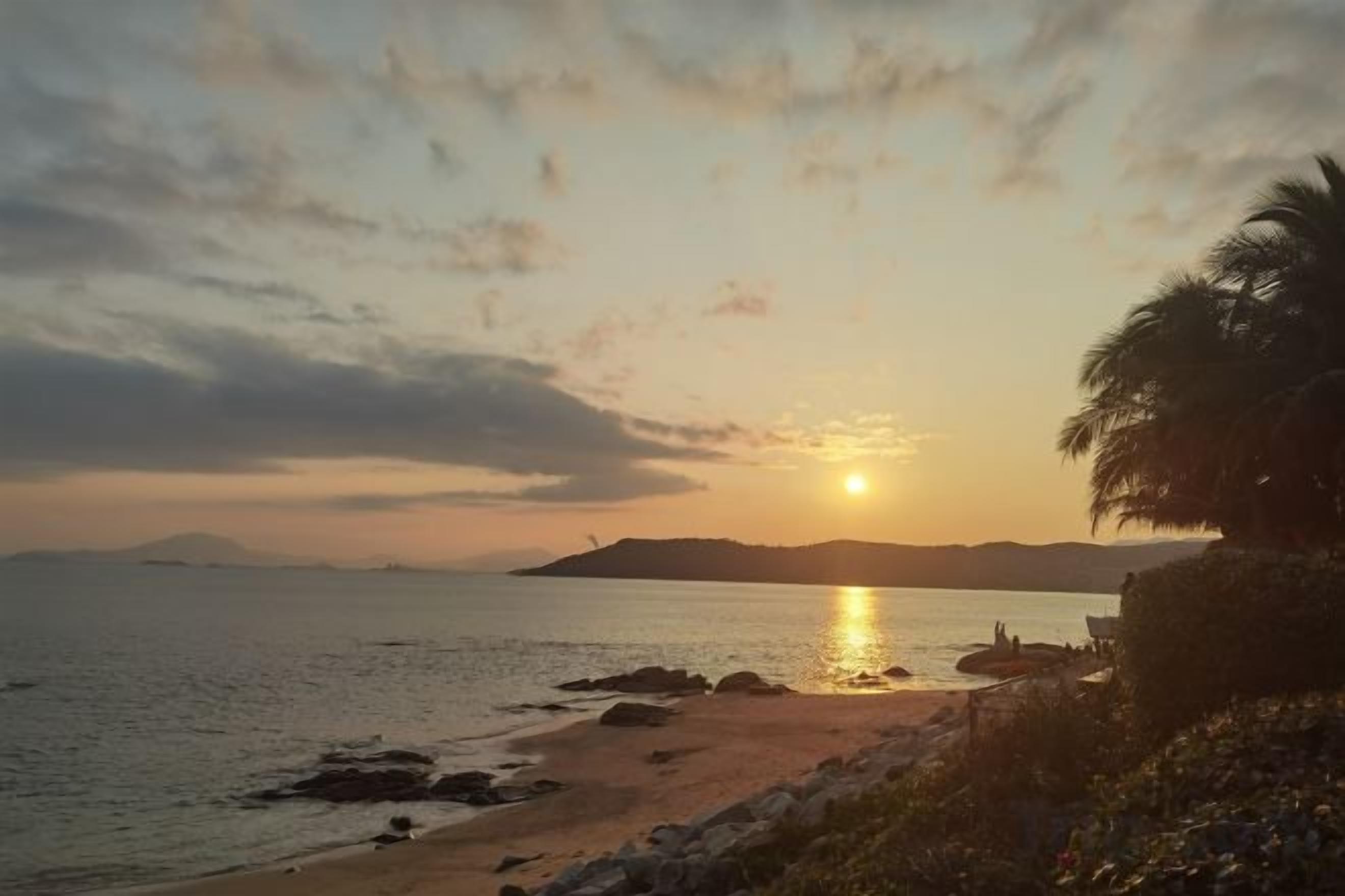 A beach scene with a sunset, calm sea, and distant land.