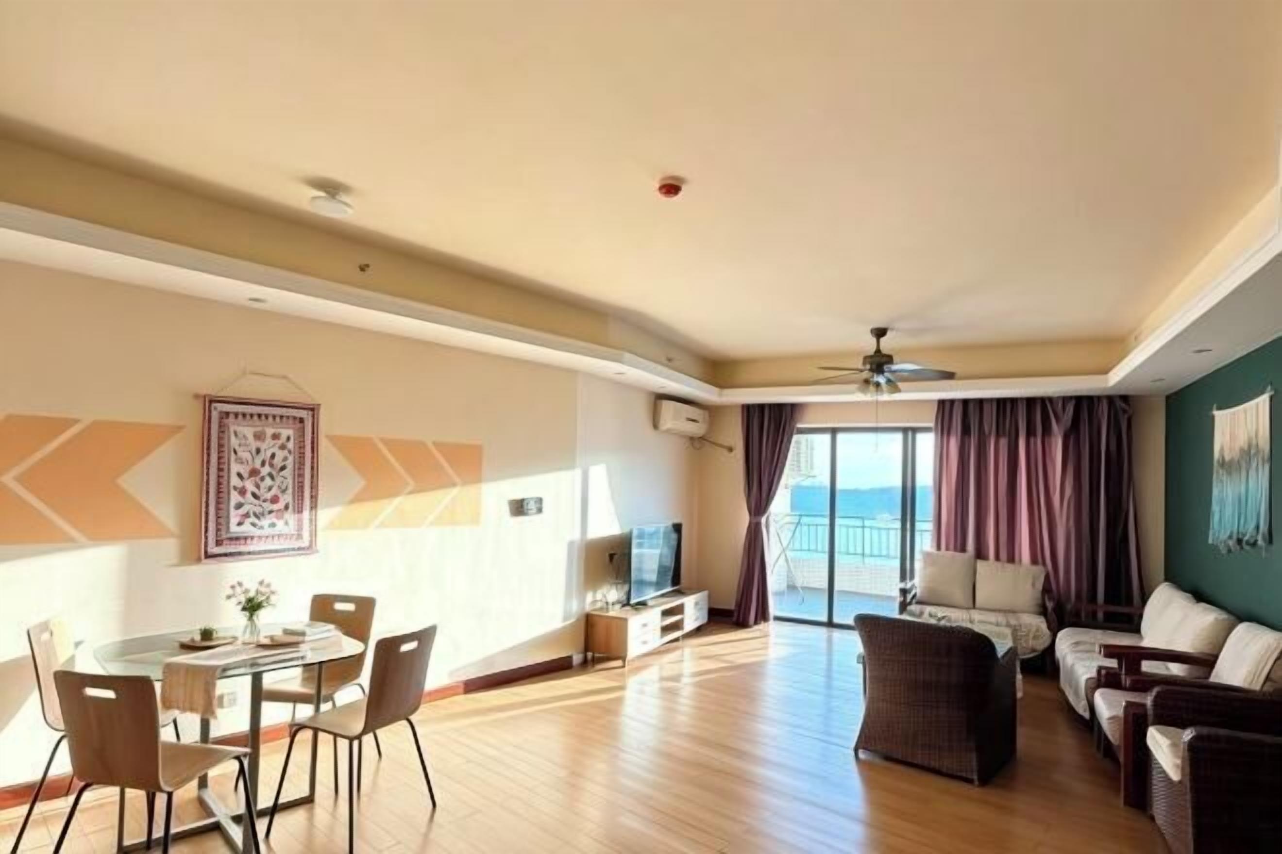 A spacious living room with a dining area, a flat-screen TV, and a balcony with a view.