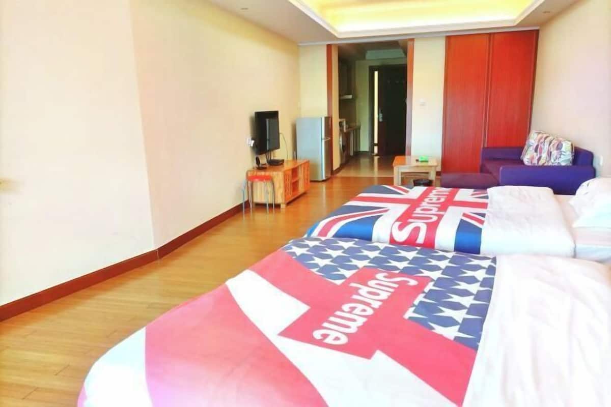 A hotel room with a bed featuring a 'Supreme' blanket, a television, a small table, and a sofa.