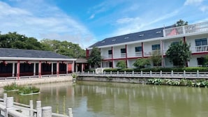 A hotel with a water body in front, a white fence, and a red and white building. - Hewu Bay Farmhouse (Shanghai)