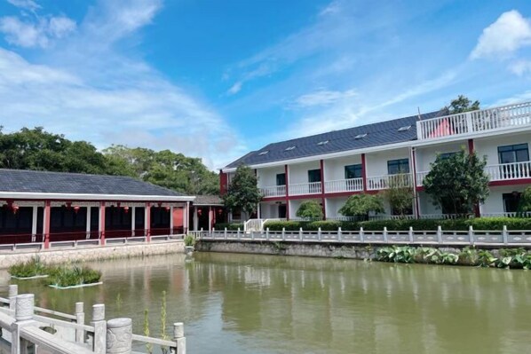 A hotel with a water body in front, a white fence, and a red and white building.