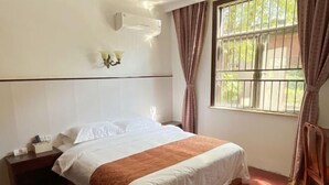 A hotel room with a bed, a nightstand, an air conditioning unit, and a window with curtains. - Hewu Bay Farmhouse (Shanghai)