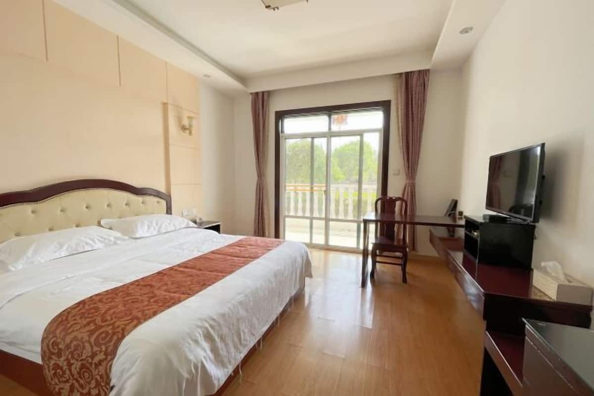 Habitación de hotel con una cama grande, un escritorio con televisor y un balcón con cortinas.