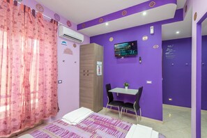 A room with a bed, a desk with two chairs, an air conditioning unit, and a television on the wall. - Grotta del Chakra (Turin)