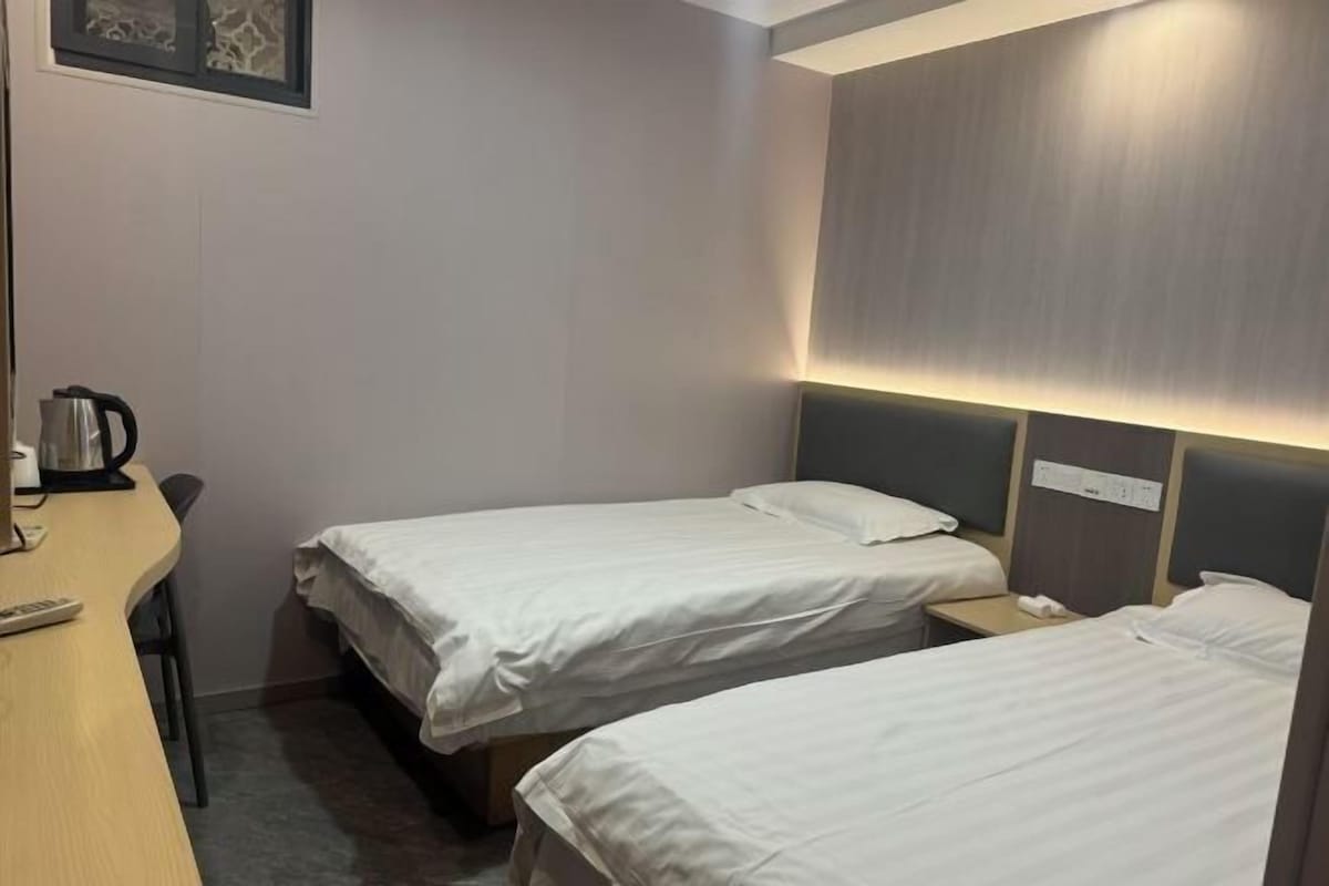 A hotel room with two single beds, a desk with a kettle, and a bedside table with a phone.